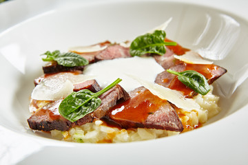 Exquisite Serving White Restaurant Plate of Risotto with Pecorino Cheese and Warm Roast Beef Close Up. Beautiful Delicacy Italian Veal Paella on Dark Stone and Leaves Background
