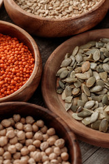 close up view of wooden bowls with chickpea, lentil, oatmeal and pumpkin seeds