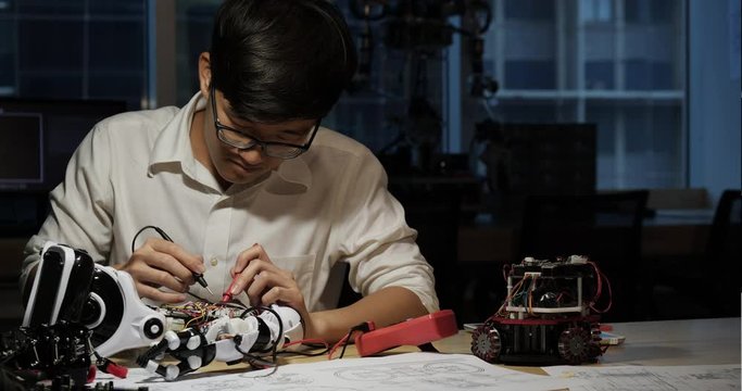 Asian engineer male assembling and testing robotics responses in laboratory.  Concept of gadget, development and productivity.