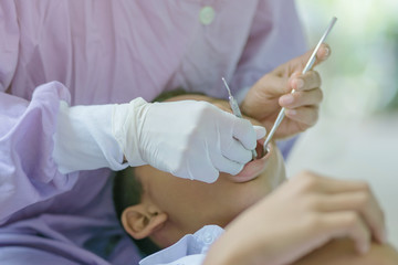 Female dentist examining teeth of a student with mouth mirror and probe checking in school.