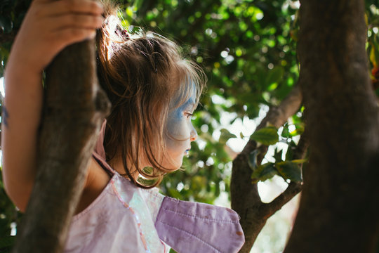 Child climbing a tree with blue face paint