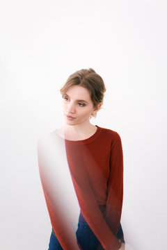 A woman in a red sweater models in front of a white wall with a light distortion in the photo