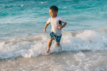 Little boy having fun running away from the saves at the beach