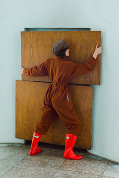 A girl in a brown overall suit holding a wooden panel