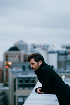 Portrait of man with black raincoat on a roof next to some buildings