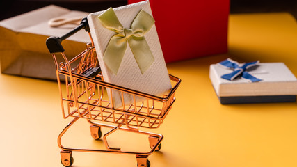 Fototapeta na wymiar Shopping cart model and gift box on yellow background