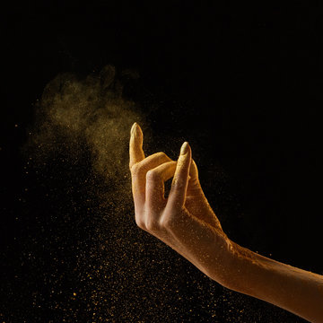A cloud of golden powder on a black background with copy space. A woman's hand pours powder. Holi holiday concept