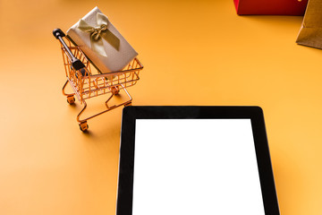 Fototapeta na wymiar Shopping cart model and tablet on yellow background