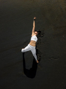 Woman doing yoga exercices on a black beach