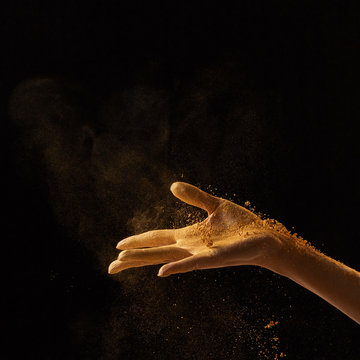 Gold dust falls on a female hand on a black background with copy space.