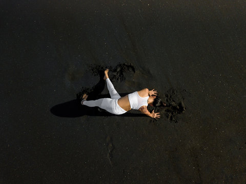 Woman doing yoga exercices on a black beach