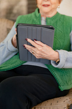 A senior woman sitting on her patio, using her tablet device.