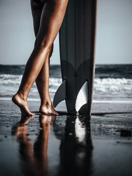 Female surfer legs next to twin fin fish surfboard standing on the beach in Sri Lanka 