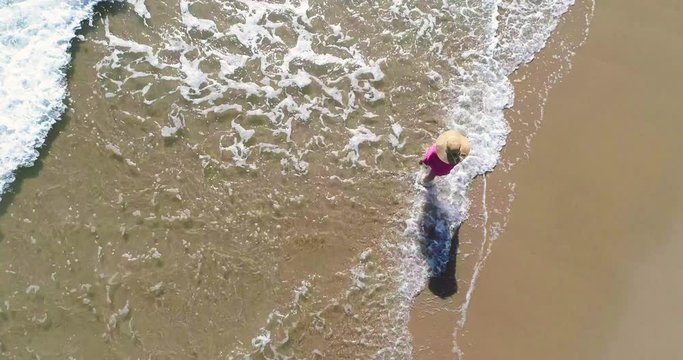 Mujer pasea sobre la orilla del mar y arena dorada y dron vuela encima