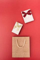 a gift box and shopping paper bag placed on a red background