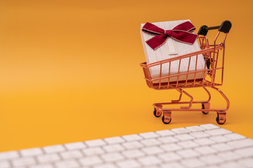 Shopping cart model and computer keyboard with gifts on yellow background