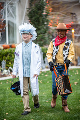 Candid photo of two of kids dressed in Halloween costumes going trick or treating outdoors in October in a decorated neighborhood
