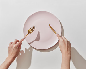 Fork and knife in women's hands with empty plate on a white background, copy space. Waiting for dinner. Flat lay