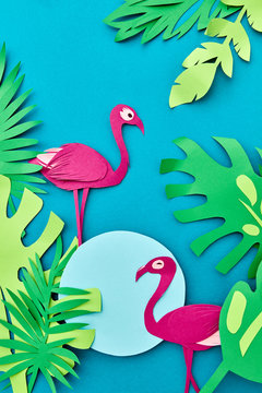 Greeting card paper handcraft frame with tropical leaves and pink flamingo on a blue background. Top view.
