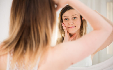 Obraz premium Portrait of girl touching face and looking at mirror in bedroom
