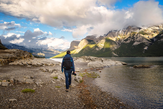 Man holding a reflex camera walking along Minnewanka lake , Canadian Rockies, Banff Alberta Canada
