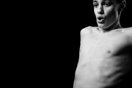 Black and white portrait of a young handsome guy with a naked torso in the studio against a dark background