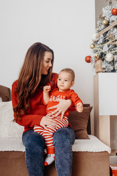 Young mother sitting on the sofa with her one year old son near Christmas tree