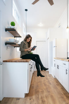 Home: Woman Sits On Counter Checking Digital Tablet