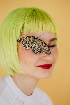 Stylish young woman with short yellow hair and butterfly sitting on her face