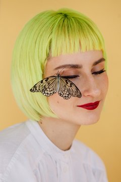 Stylish young woman with short yellow hair and butterfly sitting on her face