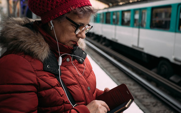 Woman standing on a subway station, waiting for metro and using a smart phone with headphone