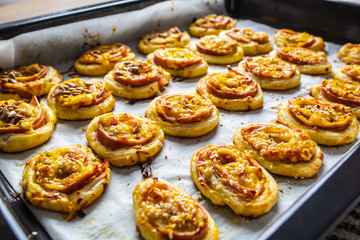 Rolls of puff pastry with ham bacon cheese sesame on baking tray