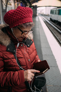 Woman standing on a subway station, waiting for metro and using a smart phone with headphone