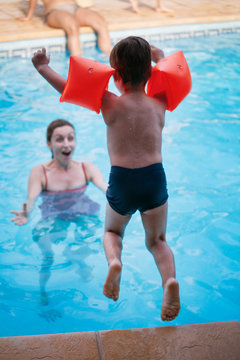 Little boy jumping into a swimmig pool with his mother