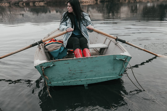 young woman wearing red rubber boots rows row boat in river