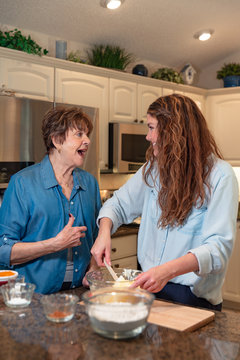 Grandmother and granddaughter laugh baking in the kitchen.