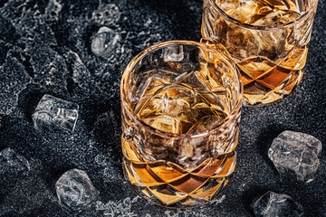 Whiskey with ice on stone dark background.