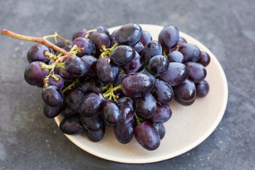 A bunch of ripe blue grapes close-up on a plate on a blue concrete shabby background