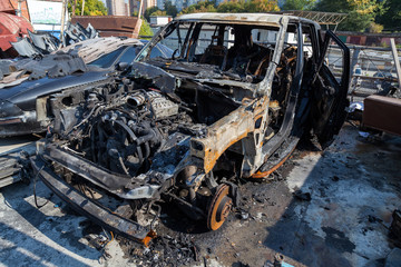 A burnt car after a fire or an accident in a parking lot covered with rust and black coal with scattered spare parts around. Robbery, arson, terrorism.