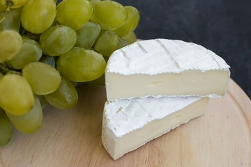 Camembert cheese and ripe green grapes on a wooden plate on a dark shabby blue concrete background