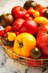 Bowl with different fresh tomatoes on light background, closeup