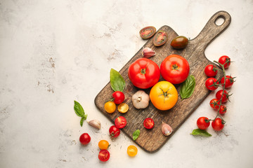 Board with different fresh tomatoes on light background