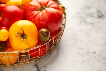 Bowl with different fresh tomatoes on light background, closeup