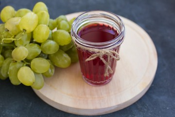 A bunch of ripe green grapes and a glass of grape juice close-up on a blue shabby concrete background.