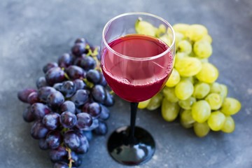 Bunches of ripe green and blue grapes and a glass of grape wine close-up on a blue shabby concrete...