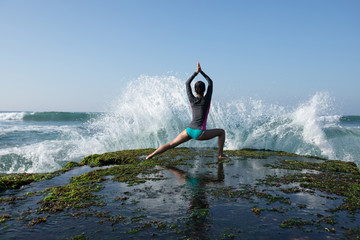 Yoga woman meditation at the seaside cliff edge facing the coming strong sea waves