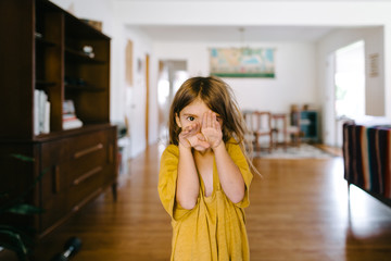 little girl in home with hands over face