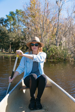 Pulled back portrait of a woman paddling in a canoe on calm lake water in Florida.