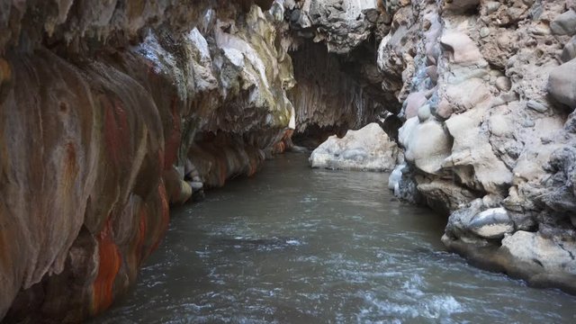 A river flowing inside an erosional cave and mineral formations on the walls