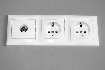 electrical outlets, a set of three white empty electrical sockets for appliances and an antenna connector for a TV on an empty gray